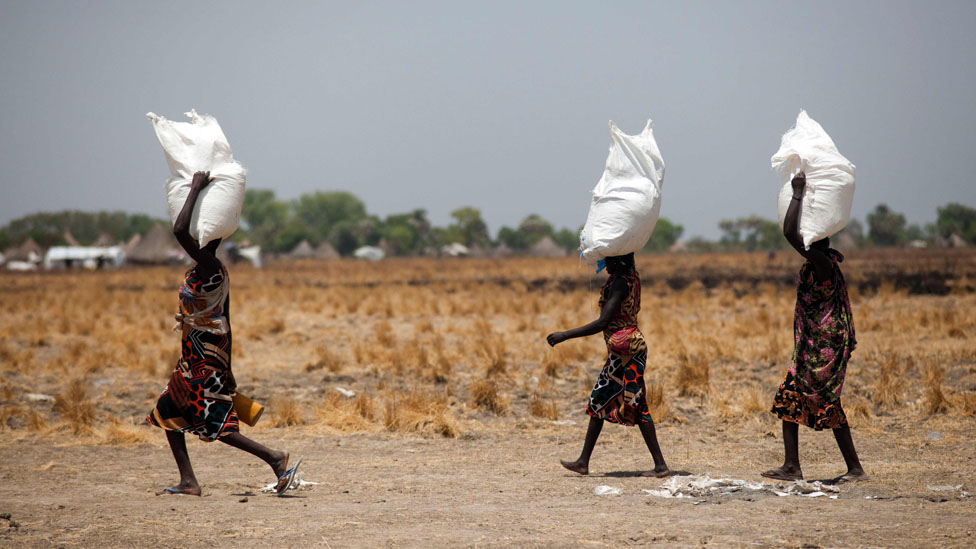 Women carry sacks across a dry landscape. Aid agencies warn that disruptions to food production and supplies could deepen hunger across Sudan and the wider region.