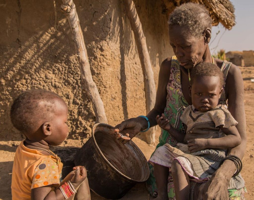 A woman sits with two young children beside a cooking pot. Children are particularly vulnerable when food shortages leave families unable to meet their nutritional needs.