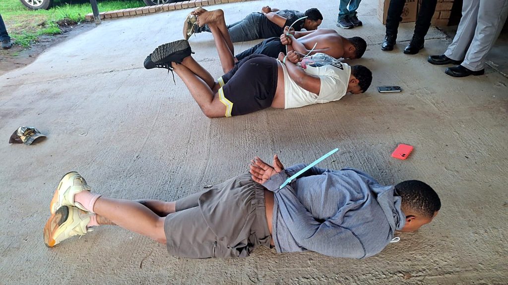 Suspects lie on the ground after their arrest during the Hekpoort raid on 8 October 2026. The five accused have not pleaded and are presumed innocent.