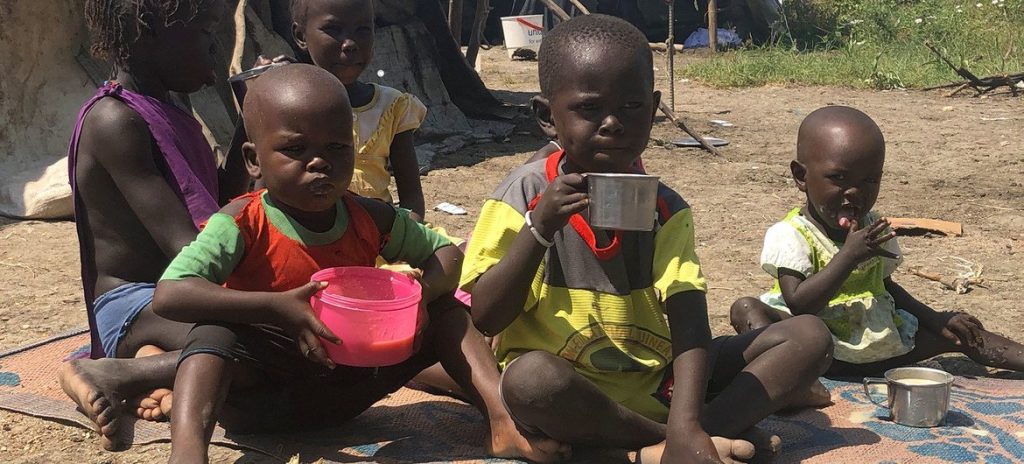 Children eat and drink while seated on a mat. UN agencies estimate that 825,000 children under five in Sudan could suffer severe acute malnutrition in 2026.