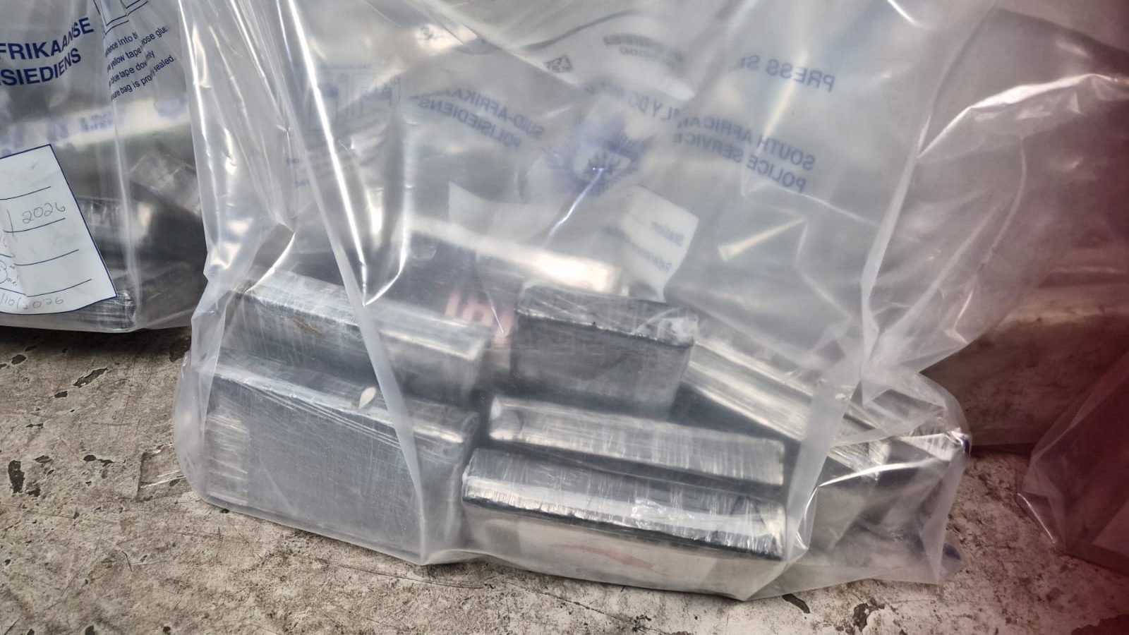 Blocks of suspected cocaine, some bearing energy-drink branding, sealed in a police evidence bag after a multidisciplinary team intercepted five luggage bags holding 216 blocks, weighing about 250kg, at OR Tambo International Airport.
