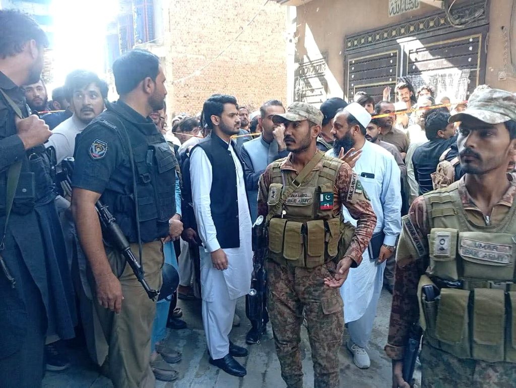 Soldiers and police guard the cordoned-off street outside the collapsed school in Peshawar as officials and residents gather nearby.